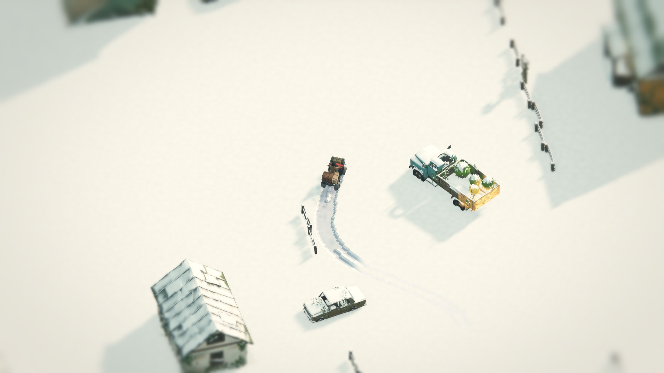 The village street under deep snow, wrecked cars snowed over, fresh quad tracks.