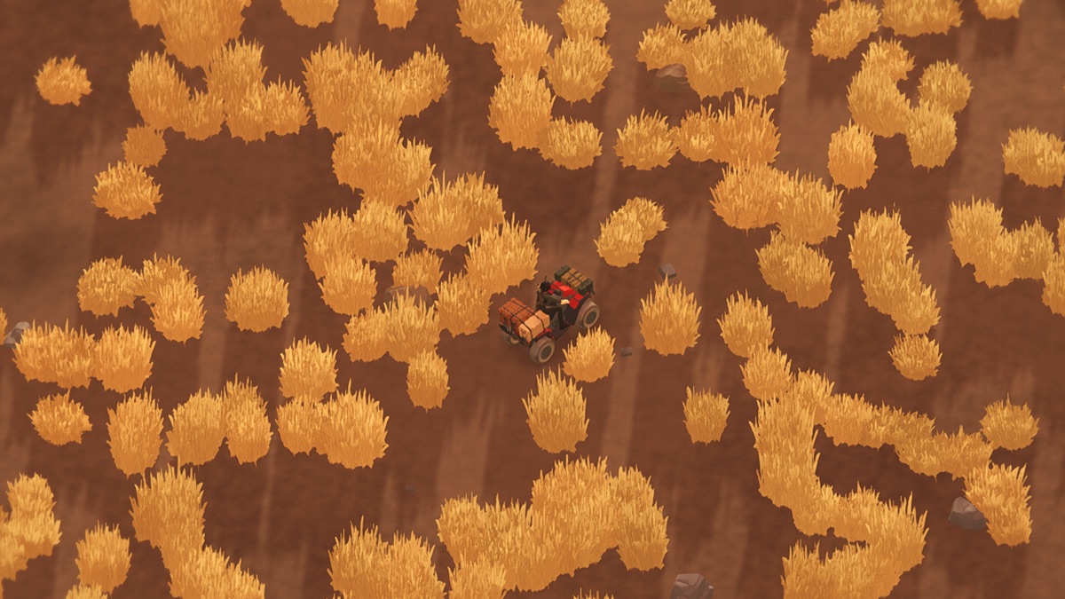 Top-down view of the quad bike on hot red-brown ground among clumps of dry gold grass, the soil bare and rust-coloured.